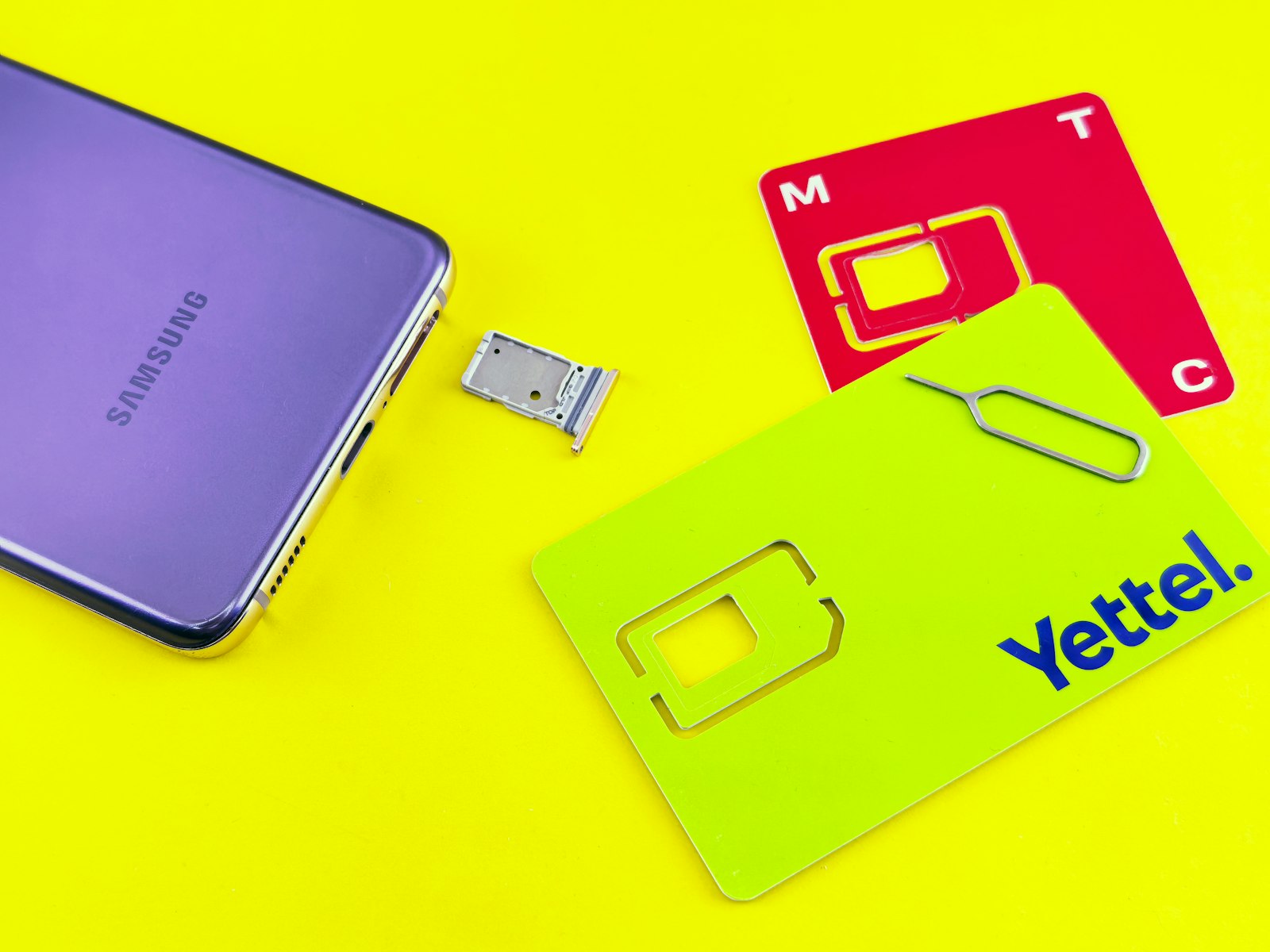 A phone, two SIM cards and a SIM tray on a yellow surface